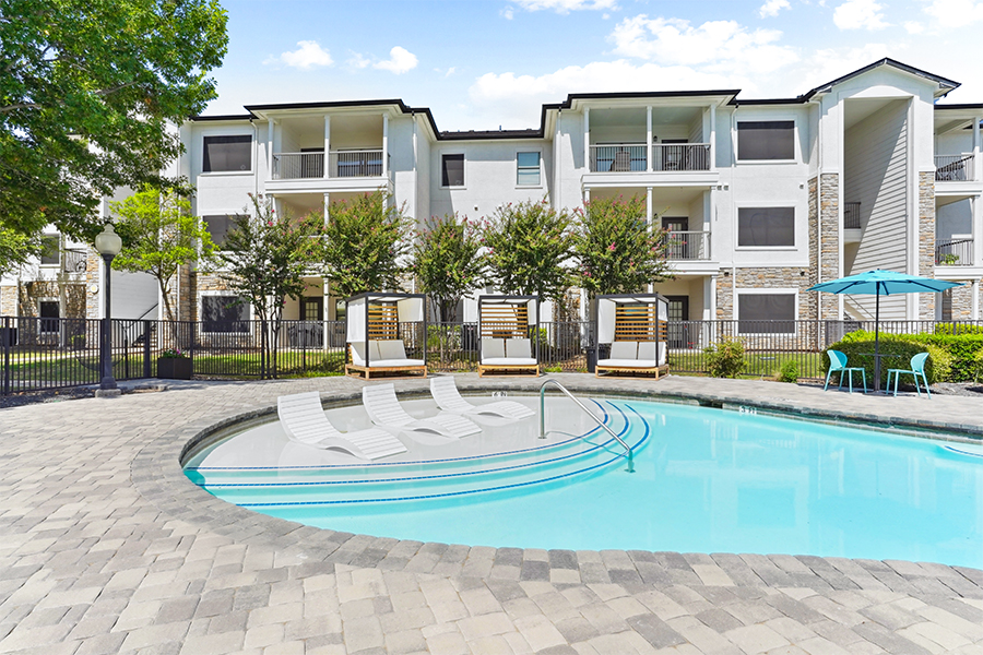 Birchstone Northlake pool with lounge chairs, umbrella and table set with apartments in the background.