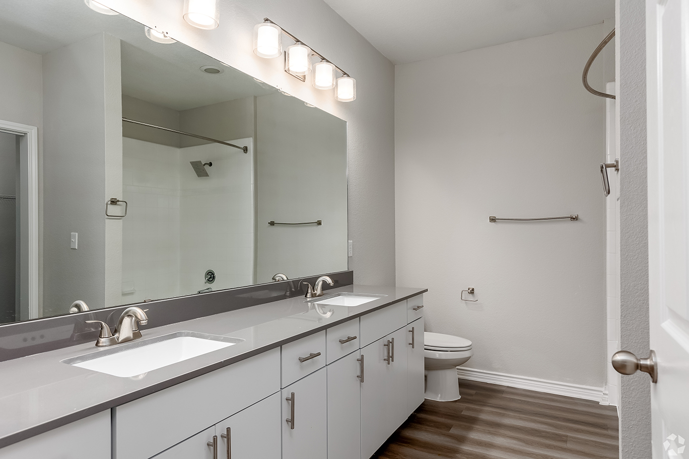 Bathroom with woodstyle flooring, white cabients, and a double vanity sink.