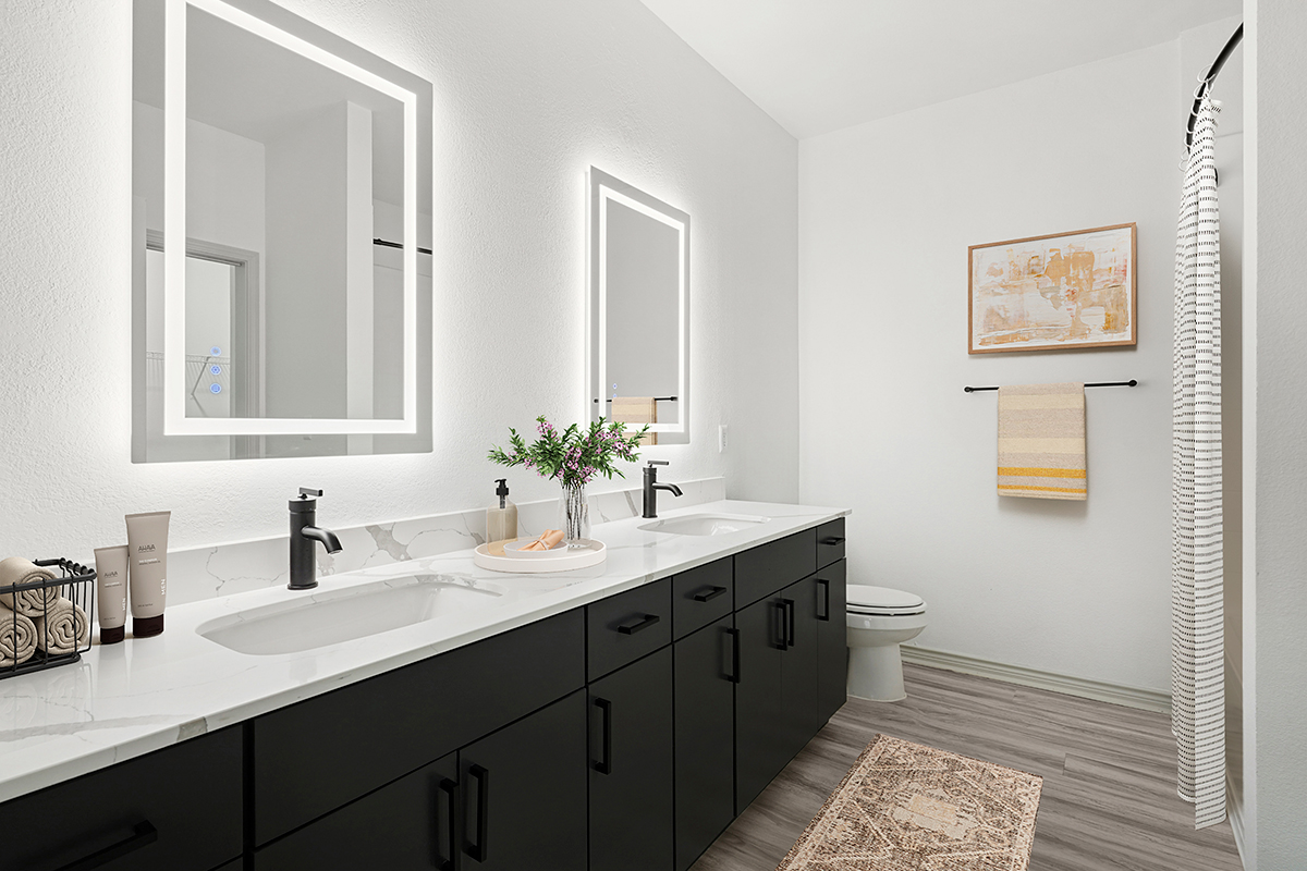 Renovated bathroom with dark cabinets, wood-style flooring, light-up vanity mirrors, quartz counters, and black fixtures.