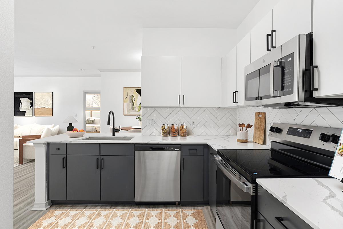Renovated kitchen with wood-style flooring, two-tone cabinets, stainless steel appliances, quartz counters and black fixtures.